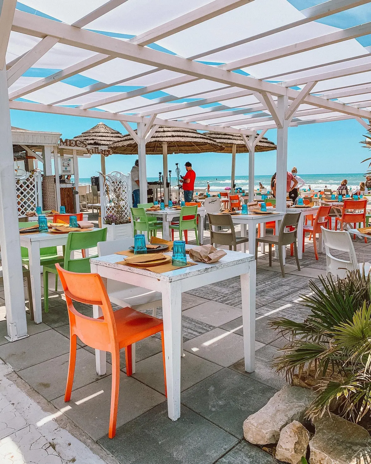 La terrazza di Mecs Village al mattino: pergolato bianco, ombrelloni di paglia e il mare sullo sfondo